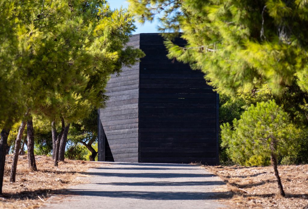 Charred-timber Dark Beacon pavilion seen from the roadway, Spetses
