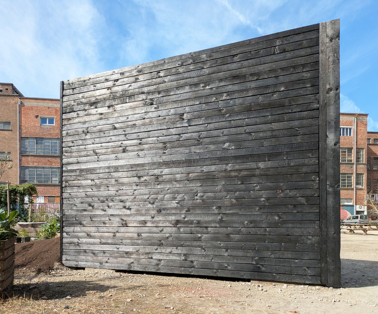 Charred-timber Plough Chapel seen from the side across the courtyard